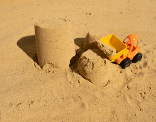 children's toy yellow-orange tractor on the beach working with sand. close up