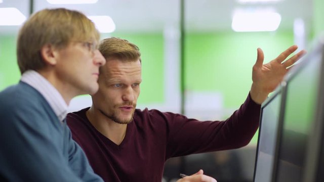 Tilt up side view medium shot of two experienced engineers looking at computer screen and discussing project in lab. Man explaining his ideas to colleague
