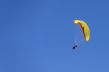 Man flying a paramotor hang glider against a blue sky