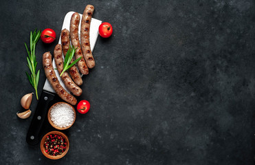 
grilled sausages with ingredients over a meat knife on a stone background with copy space for your text