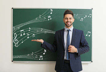 Handsome music teacher near blackboard in classroom
