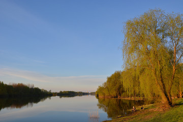 Summer landscape with a river and trees on and a fisherman in the foreground and the St. George Monastery on the horizon. Veliky Novgorod. Russia.
