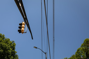 Overhead mast arm with traffic light, power lines and street light against blue sky with trees on lower border, horizontal aspect