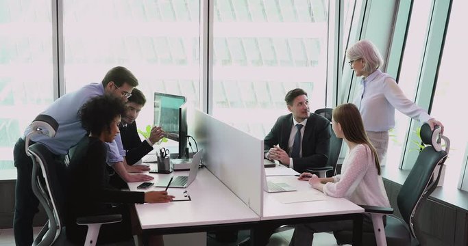 Different generations motivated mixed race business people working in small groups on project at shared office table. Young and mature diverse company managers workers employees involved in job.
