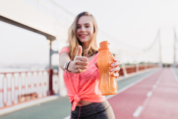 Blur portrait of stunning shapely girl posing with bottle of water. Outdoor photo of adorable woman...