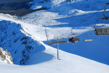 Panorama of ski resort, slope, people on the ski lift, skiers on the piste among white snow pine trees