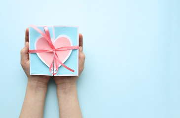 A blue greeting card with a pink paper heart and a pink tied ribbon on the palms of a Caucasian girl. Space for text. Selective focus. copy space. Valentine's day or mother's day greeting card