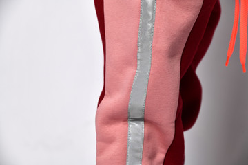 Cropped photo of a girl in pink warm sweatpants. She put one hand in her pocket, posing against a white studio background. The concept of childhood, fashion, advertising and sports.