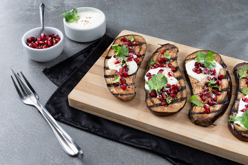 Eggplant with yorgut pomegranate seeds, nuts and parsley. Served in bamboo wood on a gray concrete background.
