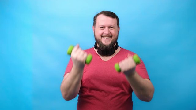 Thick bearded nice bodybuilder in pink T-shirt with very small dumbbells is very tense doing exercises