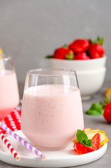 Strawberry smoothie or milkshake with banana in a glass on a gray concrete background. Summer cold drink. Vertical orientation. Copy space.