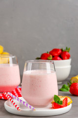 Strawberry smoothie or milkshake with banana in a glass on a gray concrete background. Summer cold drink. Vertical orientation. Copy space.