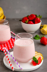 Strawberry smoothie or milkshake with banana in a glass on a gray concrete background. Summer cold drink. Vertical orientation. Copy space.