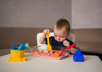 a small boy sits at a table and plays in the sand. Sensory development games for children. Games with kinetic sand at home.