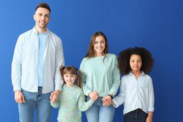 Happy couple with little adopted children on color background