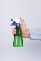 Green spray bottle in mens hand. White background. Side view