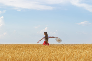 Young woman walks through wheat field with hat in hands and enjoying Sunny day. Freedom and rest