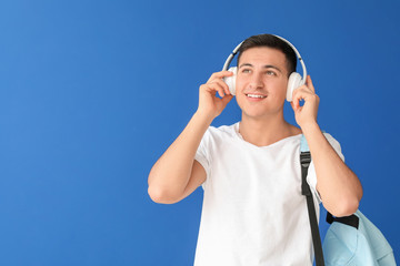 Portrait of male student listening to music on color background