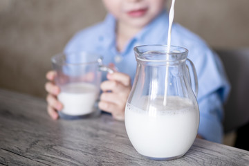 Close-up of a glass jug into which milk spills. Milk flows beautifully in a fine stream.