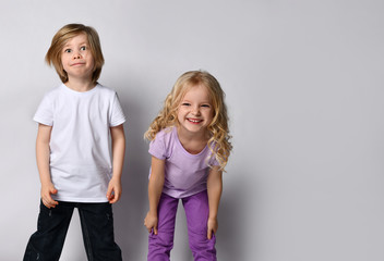 Little blonde girl in purple t-shirt and pants and boy in black and white casual clothes. They smiling, posing isolated on white