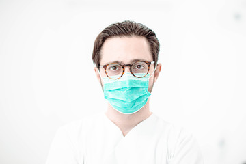 Male doctor with glasses and a mask in a white medical office looks at the camera. Portrait of a professional.