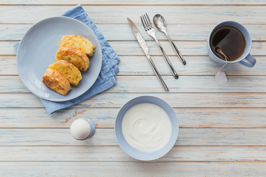 Breakfast with fried croutons, yogurt and black tea on light wooden background. Summer country food.
