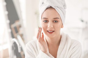 Beautiful young woman applying cream in bathroom