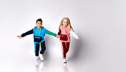 Children, boy and girl, in colorful sport suits and sneakers. They are holding hands, running, isolated on white studio background