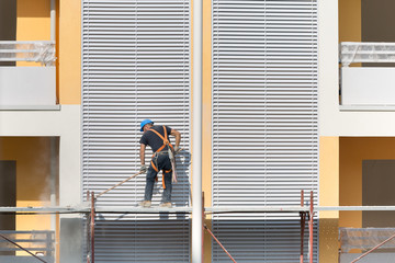 Worker with Blue Hardhat at Work on a Scaffold in a Building Site for the Construction of a Building
