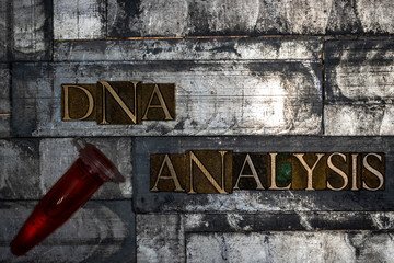 Photo of real authentic typeset letters forming DNA Analysis text with fluid filled laboratory vial...