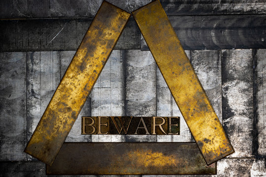 Photo of real authentic typeset letters forming Beware text on vintage textured grunge silver and copper background
