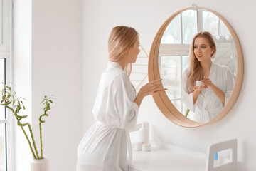 Beautiful young woman applying cream in bathroom