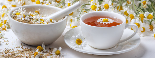 Rural still-life - cup of brewed chamomile tea on the background of a bouquet of daisies, closeup