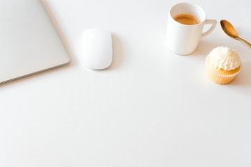 Cup of coffee and cupcake, silver laptop on white desk. Coffee break in home office concept. 