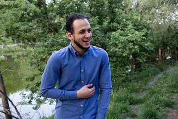 Face closeup of the young man from Middle Eastern is laughing during dialog. Closeup portrait of a man from Egypt in blue shirt in the park.