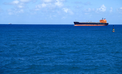 A tanker cargo ship on the sea, passing by a cardinal navigation buoy.