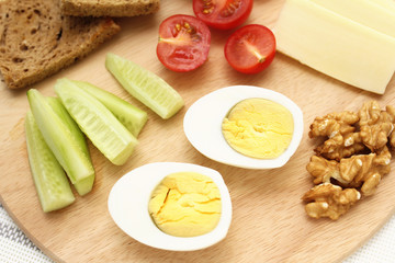 boiled egg, cut in half, cucumber wedges, cheese wedges, toast, healthy food on a breakfast board