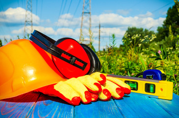 Protective helmet, headphones, gloves on a wooden table, against the background of nature and high voltage posts..