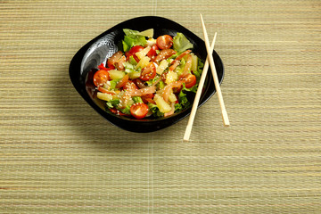 Pan-Asian salad with chicken and pineapple in a black plate on a bamboo mat and chopsticks.
