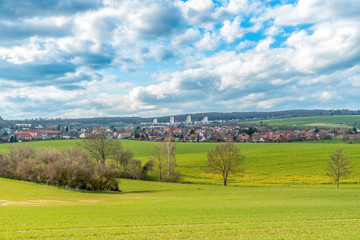 A landscape with meadows and fields in the background are three skyscrapers. The sky is drawn through