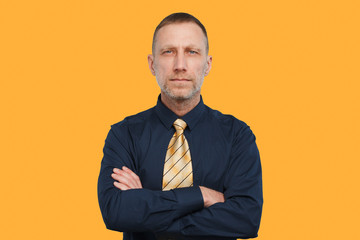 Man in a dark blue shirt and a bright yellow tie and with arms crossed on an orange background