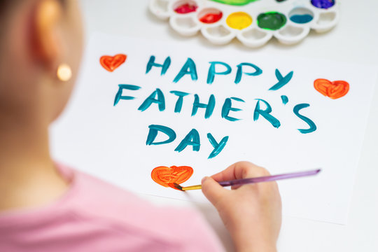 Child is drawing red heart with text Happy Father's Day on white paper. Happy Father's Day concept.