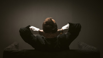 Businessman pondering new startup project sitting on a sofa. Rear view of Man in black suit sitting...