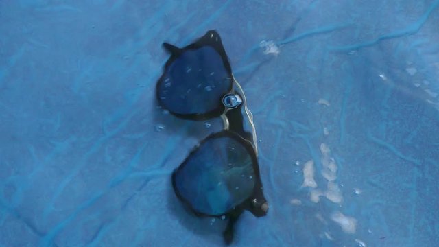 A blue sunglass dipped in the deep water of pool and stream going over it.