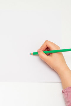 Top view of girl's hand drawing on white blank paper by green pencil. Mockup. Empty space for text.
