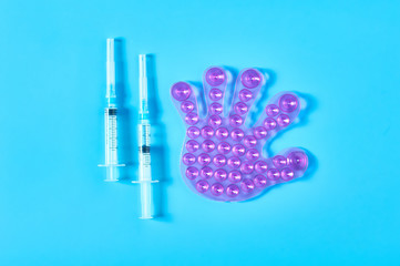 One rubber toy human palm with many suction cups near syringes on blue background. Healthcare concept