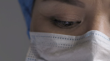 Tired doctor's eye. Woman in protective mask looks down, young woman exhausted from overworking during coronavirus pandemic, close up of female medic eye. Copy space at left side