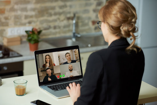 A Laptop Screen View Over A Woman's Shoulder. A Girl Works Remotely On A Computer In Her Studio. A Female Professor Listening To The Answers Of The Students In An Online Lesson At Home.