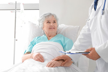 Male doctor working with elderly patient in hospital room