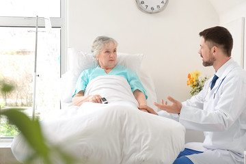 Male doctor working with elderly patient in hospital room